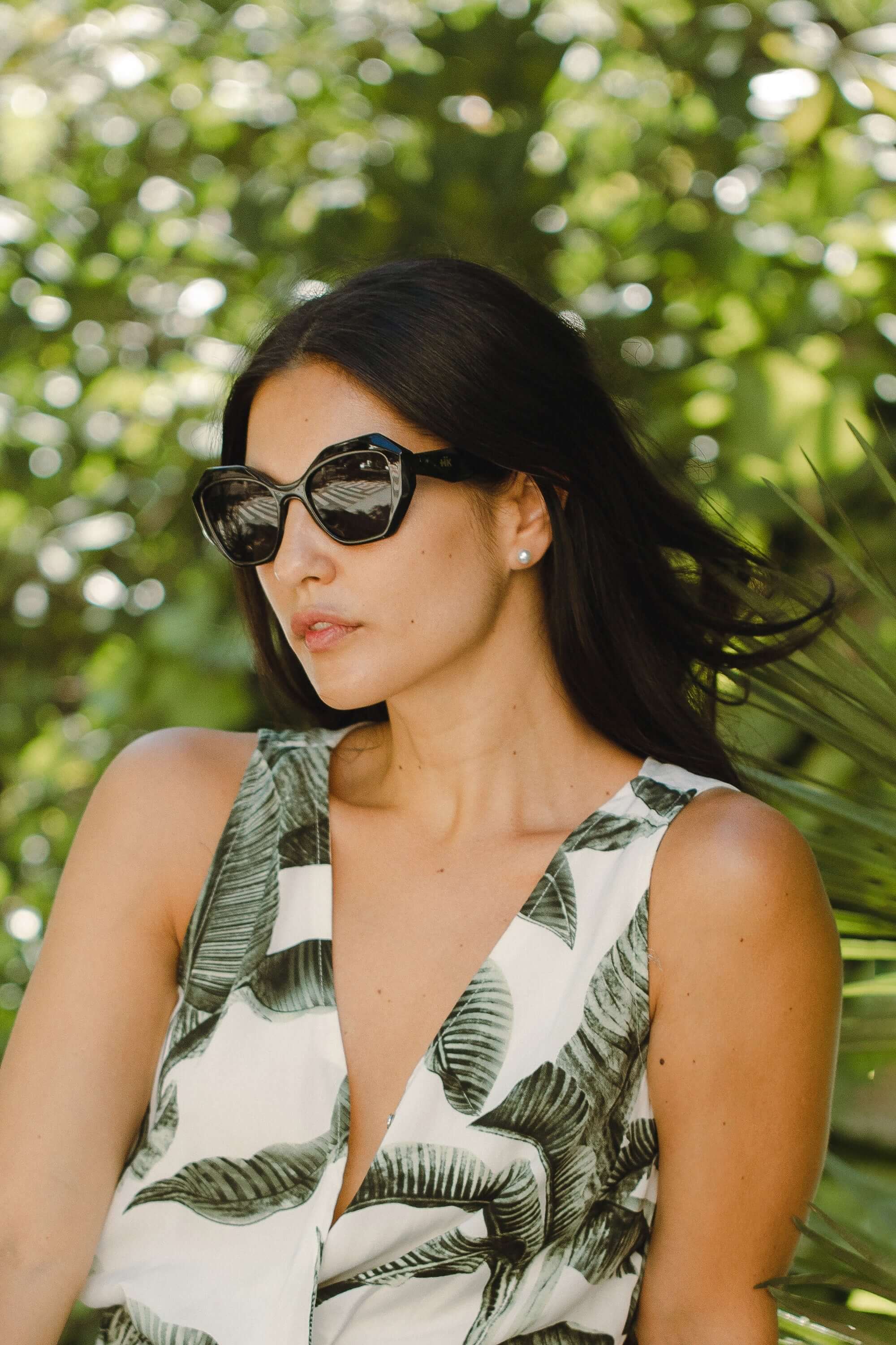 Mujer usando gafas de sol Hanukeii® Moorea Black / Black con fondo de hojas verdes.