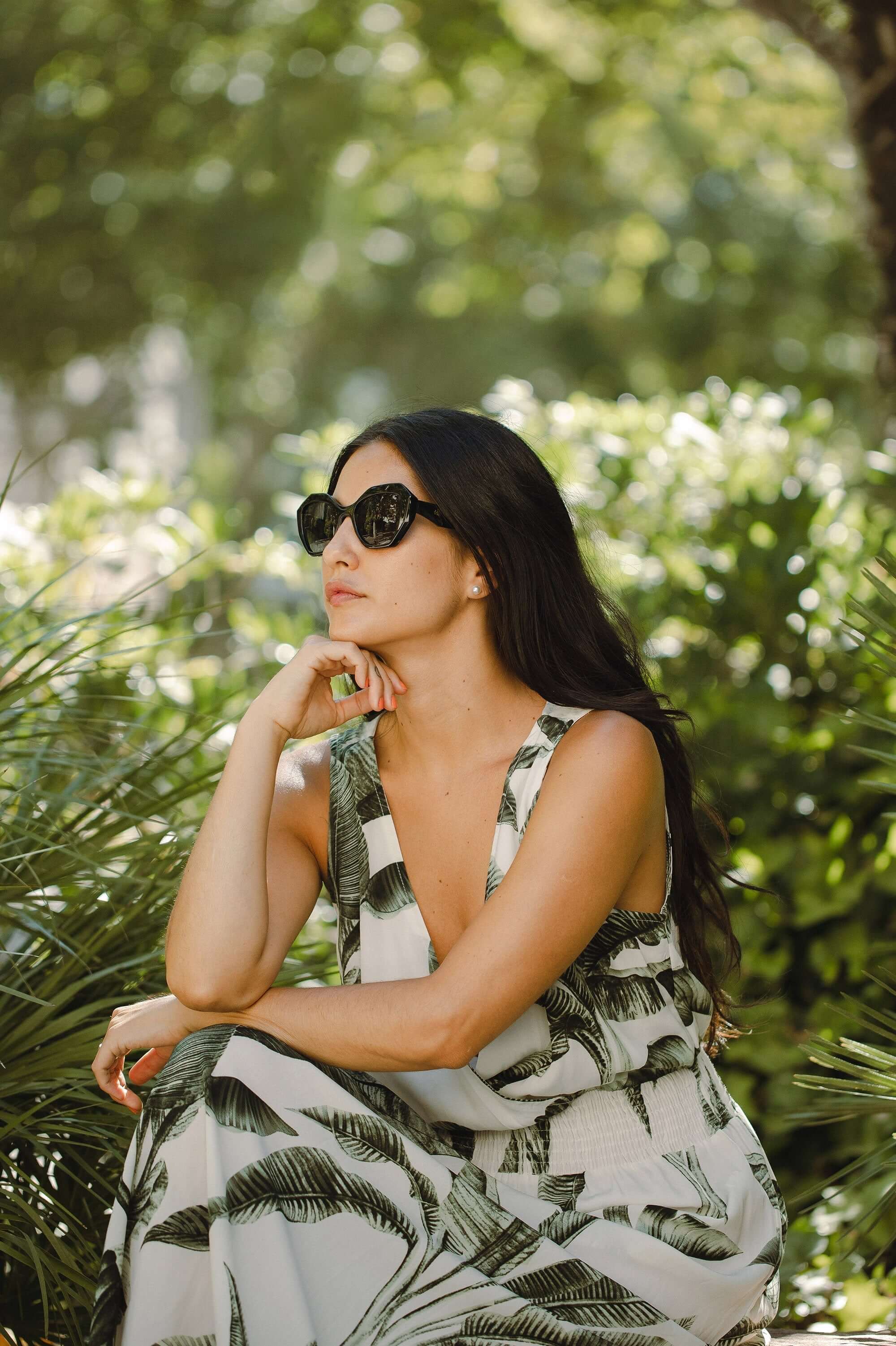 Mujer con gafas de sol Hanukeii® Moorea Black / Black, sentada en un entorno natural con plantas verdes.