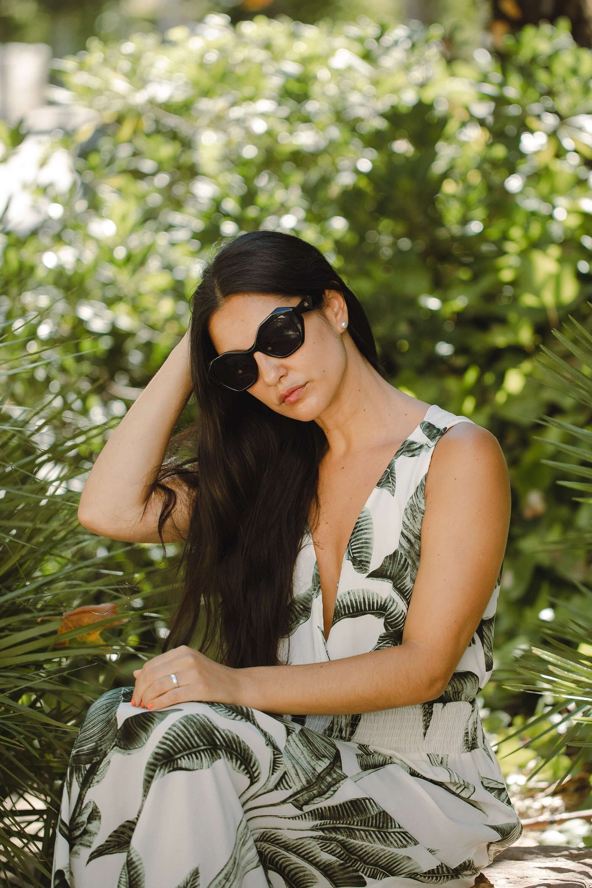 Mujer con gafas de sol Hanukeii® Moorea Black / Black sentada entre plantas verdes.